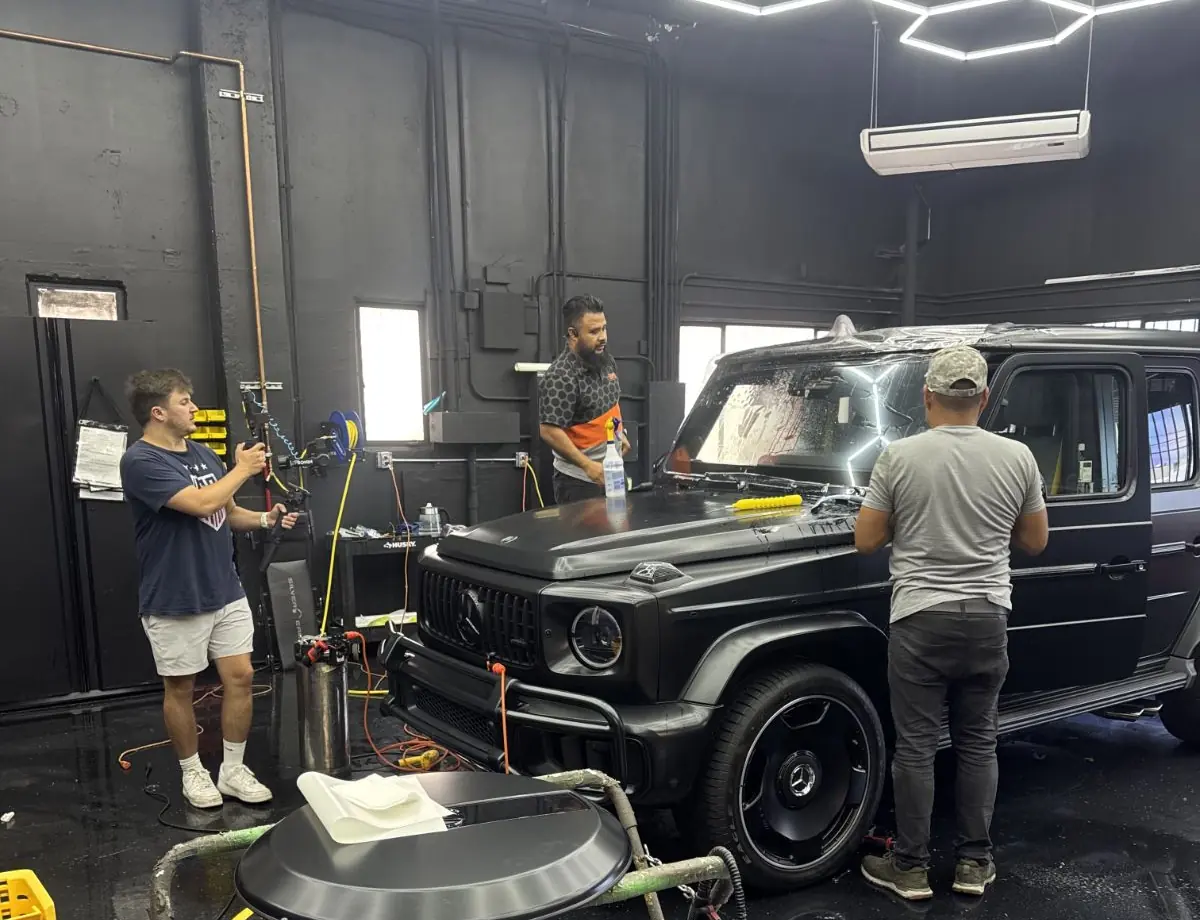 Three SFS Bay Area installers working on a Mercedes-AMG G63 under hexagonal LED lighting in the San Jose installation bay